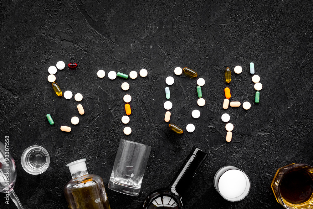 Obraz premium Stop alcohol. Word stop lined with pills near glasses and bottles on black background top view copy space