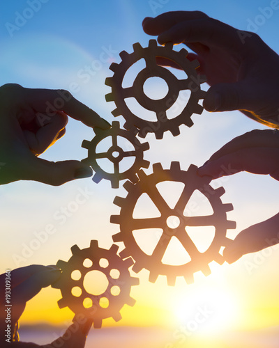 Four hands of businessmen collect gear from the gears of the details of puzzles. against the background of sunlight. The concept of a business idea. Teamwork. strategy, cooperation. Close-up