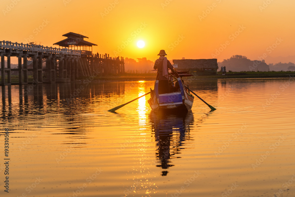 Burmese boatman and buddhist novice sitting in boat, morning sunset in U Bein bridge, Mandalay, Myanmar
