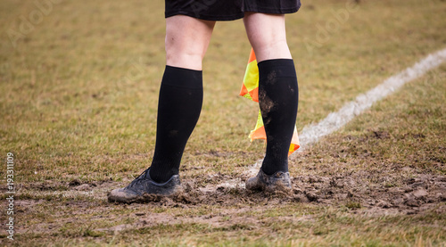 Soccer referee assistant stands at corner side with flag at hands. Blur green field background, close up.
