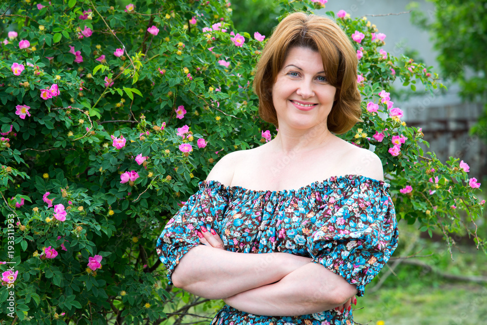 Smiling woman standing near blossoming dog rose
