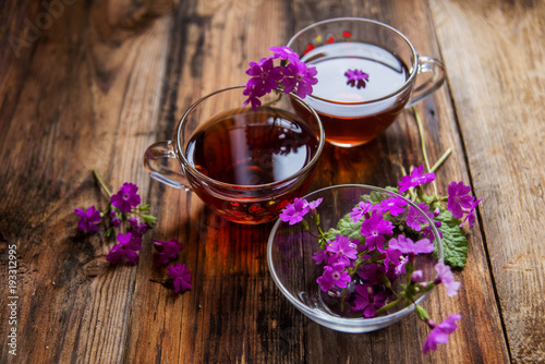 Glass cup of tea on old wooden surface. Small white flowers.