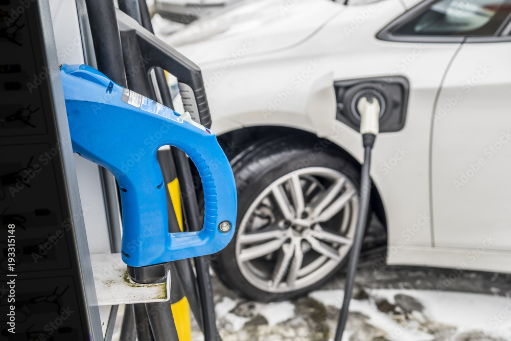 View of an Electric Car Charging and in the background a partial view of a car View of an Electric Car Charging and in the background a partial view of a car