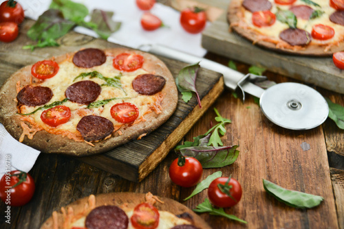 Mini Pizza With Cherry Tomatoes And Salami Sausages On A Wooden Background Natural Rustic, A Pizza Cutter And Ingridienty.