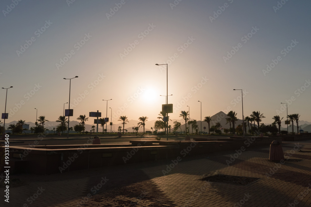 pillars of street lighting, palm trees, mountains in the backlight of the sun