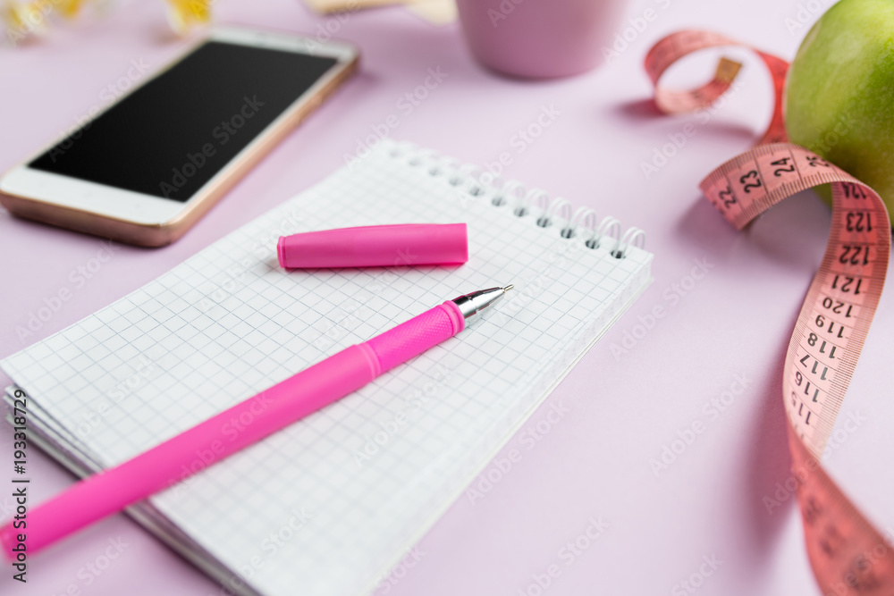 side view of green apple, measuring tape, mobile phone, pen and open notebook. Fitness Concept. side view of green apple, measuring tape, mobile phone, pen and open notebook. Fitness Concept.