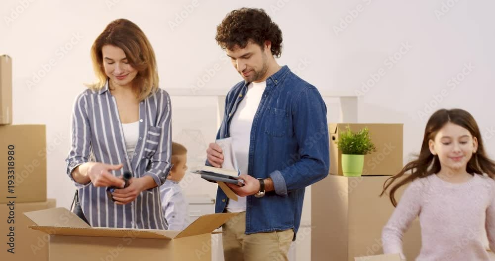 Family moving in to the new home. Mother and father unpacking boxes and their children helping them. Inside Family moving in to the new home. Mother and father unpacking boxes and their children helping them. Inside