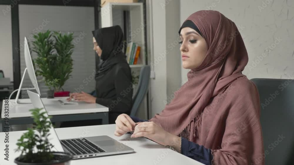 Young beautiful girl in pink hijab puts on glasses and starts working on the computer. Arab women in the office 60 fps
