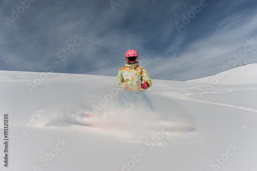 Female snowboarder in pink helmet and glasses riding down the mountain slope