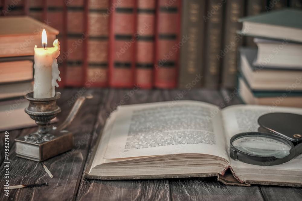 Naklejka premium On the wooden background of the table there are stacks of colorful books near the old candlestick with burnt matches lying next to each other.