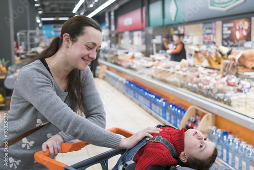 A young woman with a small son in a supermarket. The boy sits in a baby cart and laughs photo