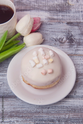 Plate with delicious doughnut with white Crea mIcing  and beautiful Tulip flowers on Rustic grey background with copy space for Text. Vertical image.