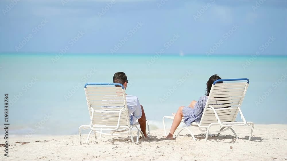 Happy couple relaxing on a tropical beach on sunbed Happy couple relaxing on a tropical beach on sunbed