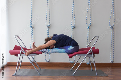 Fotografía Female yoga instructor using two chairs as props to practice forward bend asana