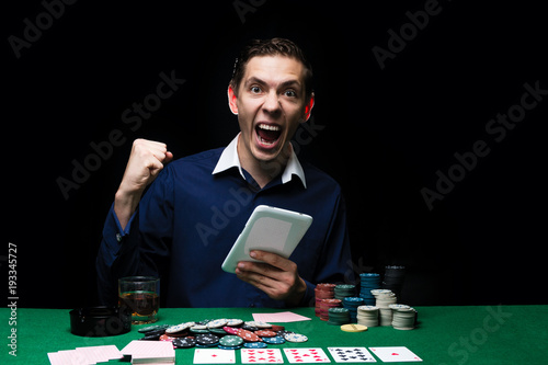 Man is playing poker with tablet online. Emotional card player win in game, man very happy with making right choices, winning all the chips on bank. Concept of victory and internet online game