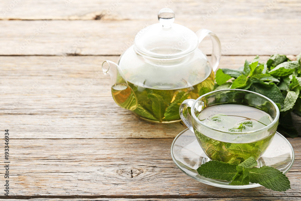 Cup of tea and teapot with mint leafs on wooden table Cup of tea and teapot with mint leafs on wooden table