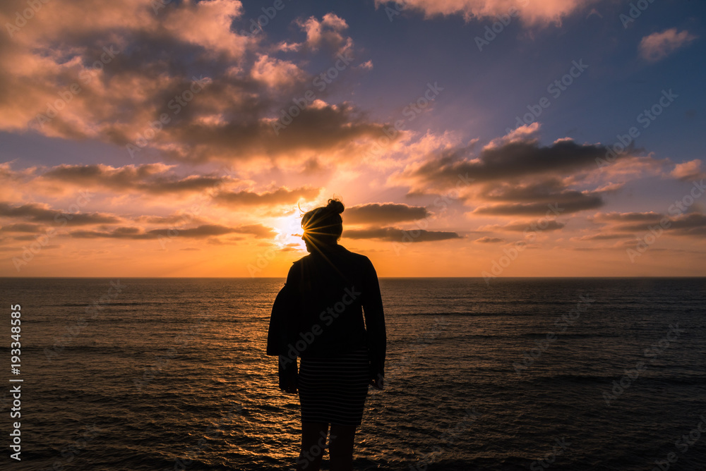 Fototapeta premium Silhouetted woman at sunset on cliff over ocean
