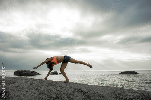 Woman doing a handstand on a rock at sunset on Bakovern Beach, Cape Town.