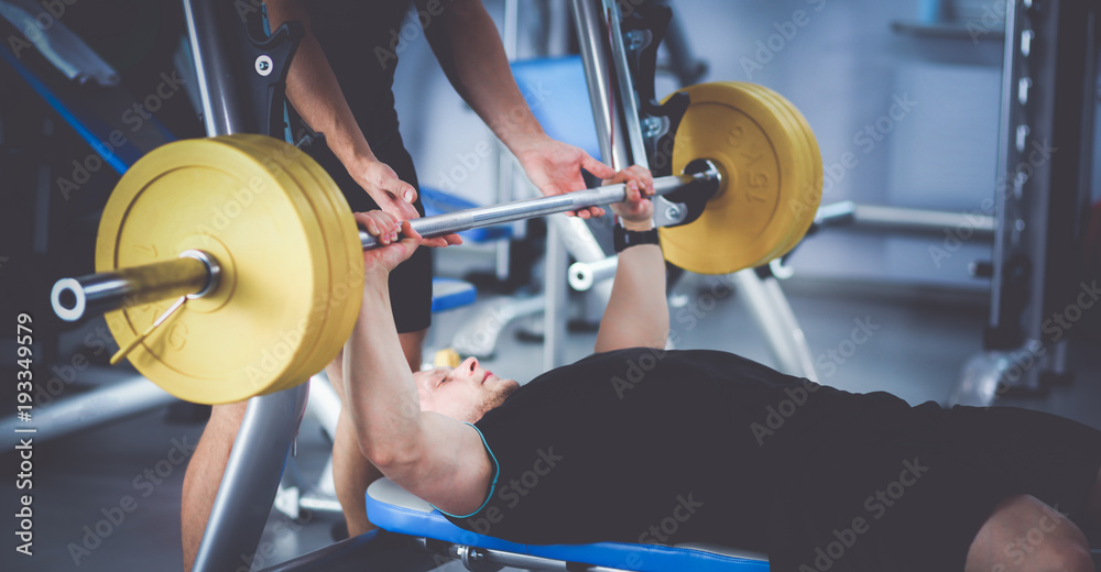 Fototapeta premium Young man lifting the barbell in gym with instructor