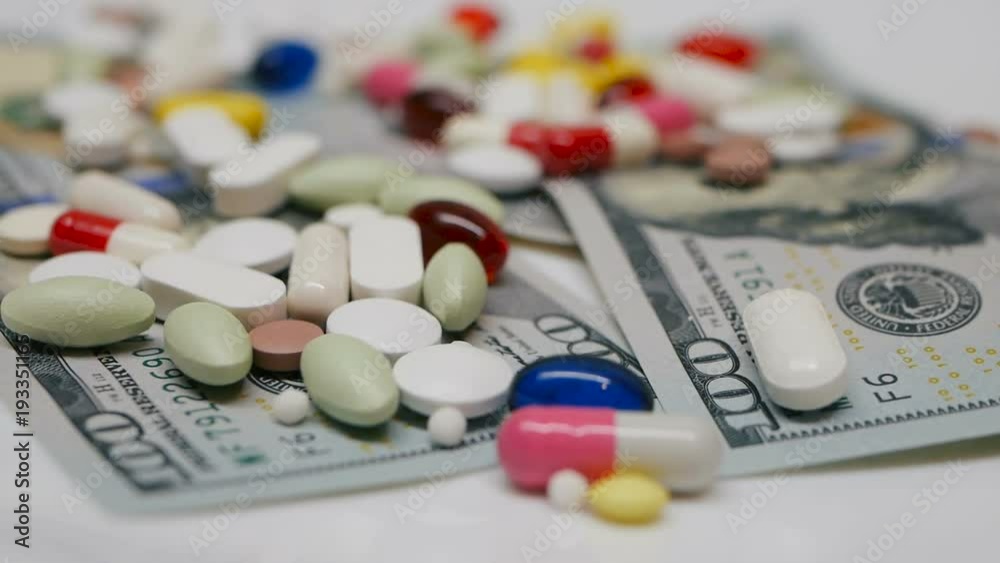 Close up, with red, white, colored pills rotating on dollars banknotes on white backgrounds Close up, with red, white, colored pills rotating on dollars banknotes on white backgrounds