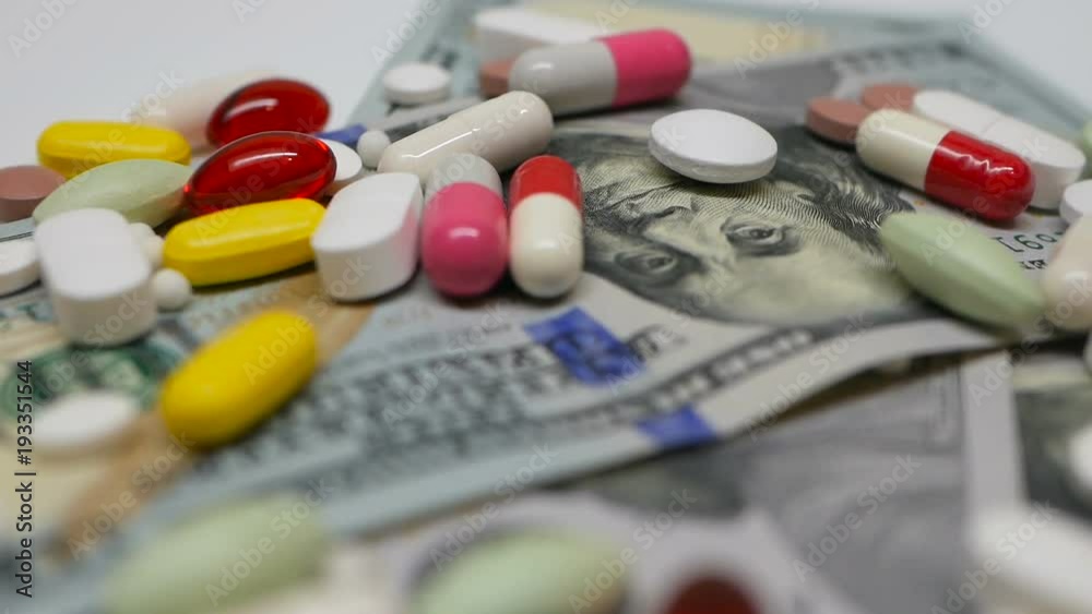 Close up, with red, white, colored pills rotating on dollars banknotes on white backgrounds Close up, with red, white, colored pills rotating on dollars banknotes on white backgrounds