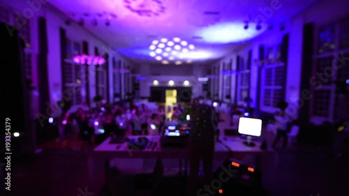 Defocused rear view of music DJ mixing dancing in front his turntables and mixer and laptop during party wedding - illumination laser light of his back large room macarena dancing guests