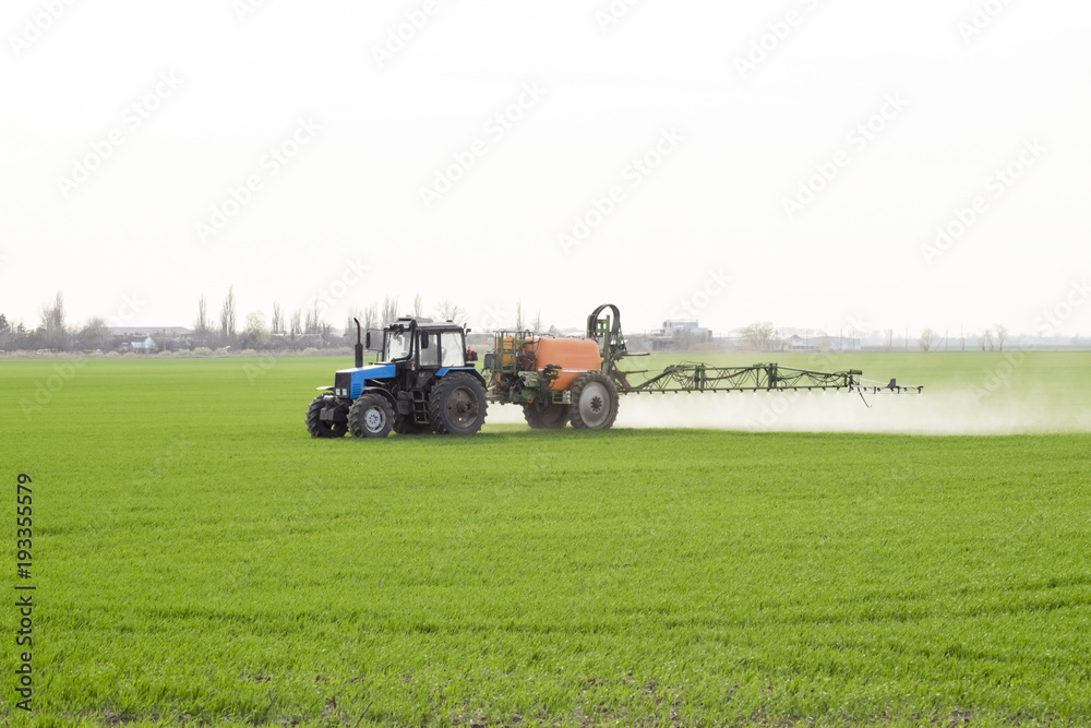 Tractor with high wheels is making fertilizer on young wheat. The use of finely dispersed spray chemicals. Tractor with a spray device for finely dispersed fertilizer. Tractor with high wheels is making fertilizer on young wheat. The use of finely dispersed spray chemicals. Tractor with a spray device for finely dispersed fertilizer.