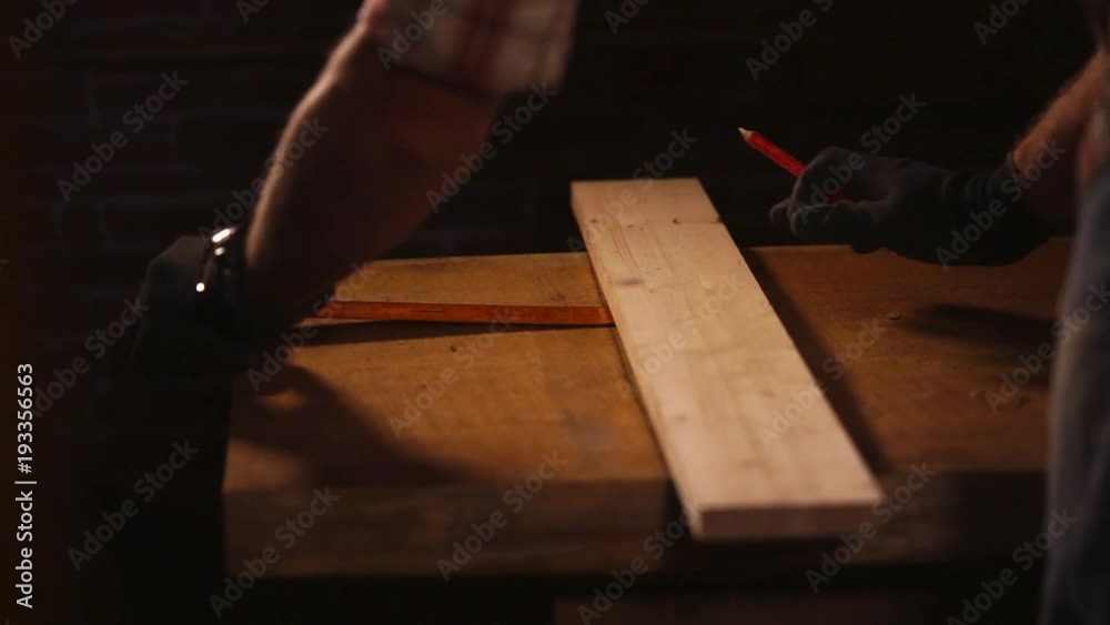 Carpenter is drawing line on a timber piece in processing workshop. He is using ruler, wooden plank and pencil, marking works Carpenter is drawing line on a timber piece in processing workshop. He is using ruler, wooden plank and pencil, marking works