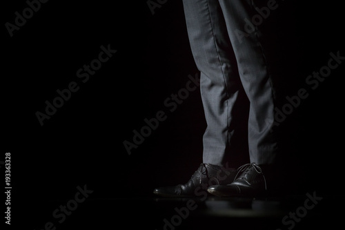 Young fashion businessman's legs in classic pants and shoes on black background.