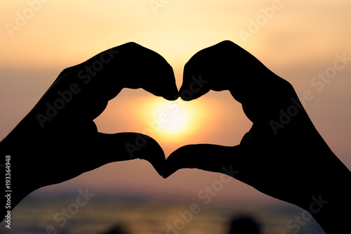 Silhouette hand in heart shape with sunrise in the middle and beach .as background Valentine concept with copy spaces for your text or design.