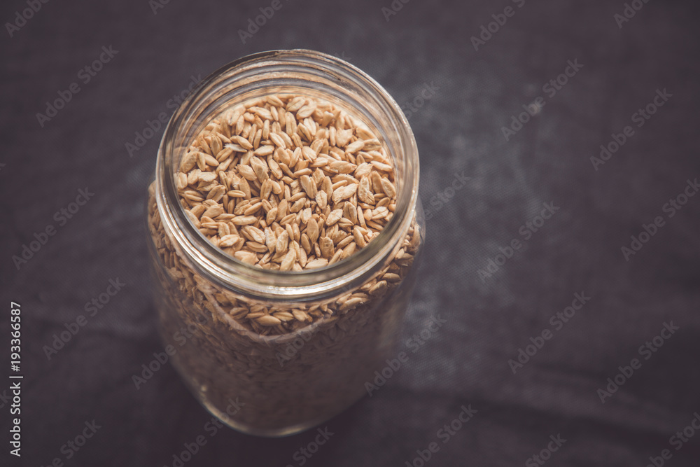 A full jar of whole organic crimped oats in a glass jar against a black linen background. A full jar of whole organic crimped oats in a glass jar against a black linen background.