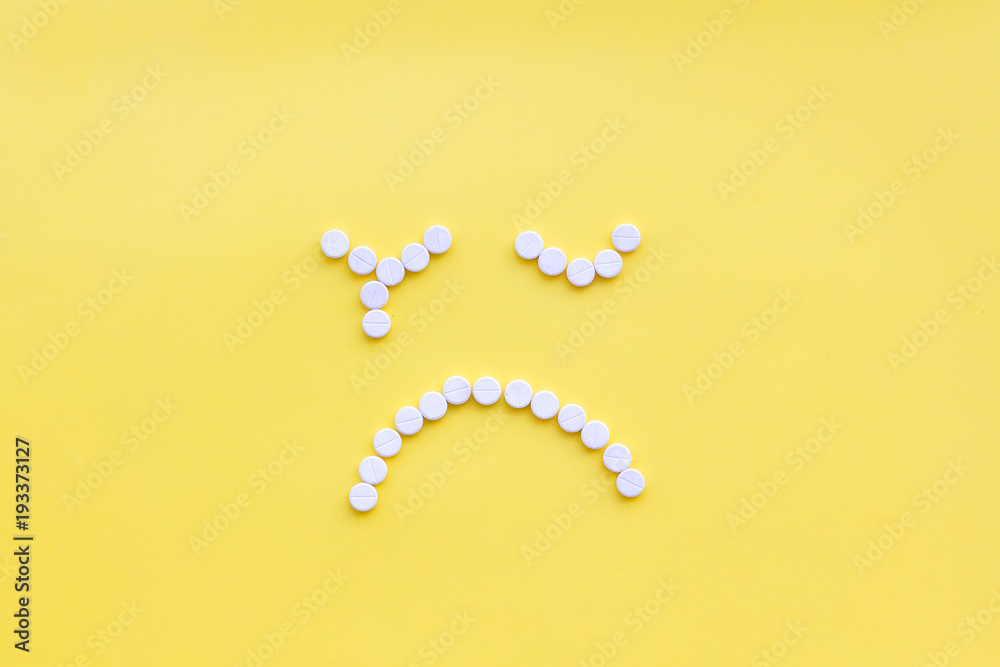 Emotion management concept. Overcome depression. Sad face lined with pills. Yellow background top view copy space Emotion management concept. Overcome depression. Sad face lined with pills. Yellow background top view copy space