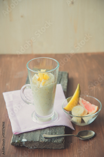 fresh smoothies in glass glass with banana, orange, mango, on wooden background.