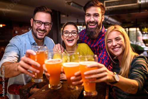 Group of young friends in bar drinking beer toasting