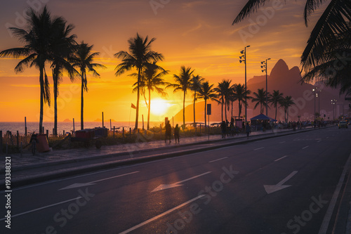 Sunset over Ipanema Beach with Dois Irmaos mountains in Rio de Janeiro, Brazil. People walking by the beach.