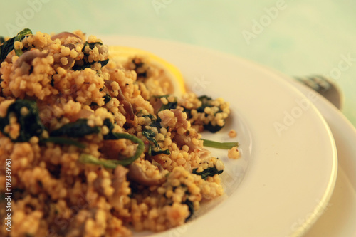 Millet with mushrooms and spinach. Close up. Vegan dish. Vegetarian couscous on the round white plate.