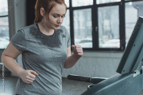 Schilderij op canvas Overweight girl running on treadmill in gym