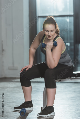Overweight girl training with dumbbell in gym