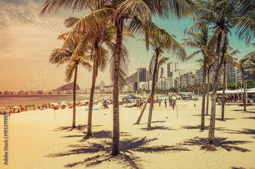 Copacabana Beach full of people view through coconut palms in Rio de Janeiro, Brazil. Light effect applied