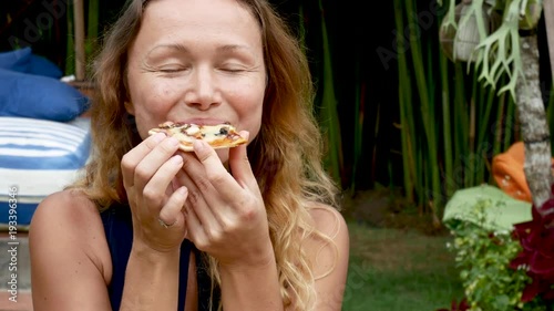 Hipster girl eating pizza and smiling to the camera in the restaurant