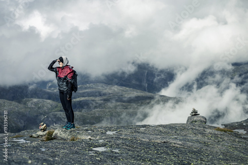 Silhouette of young woman in raincoat walking along the plateau through the foggy place on the way to Kjeragbolten, Norway.