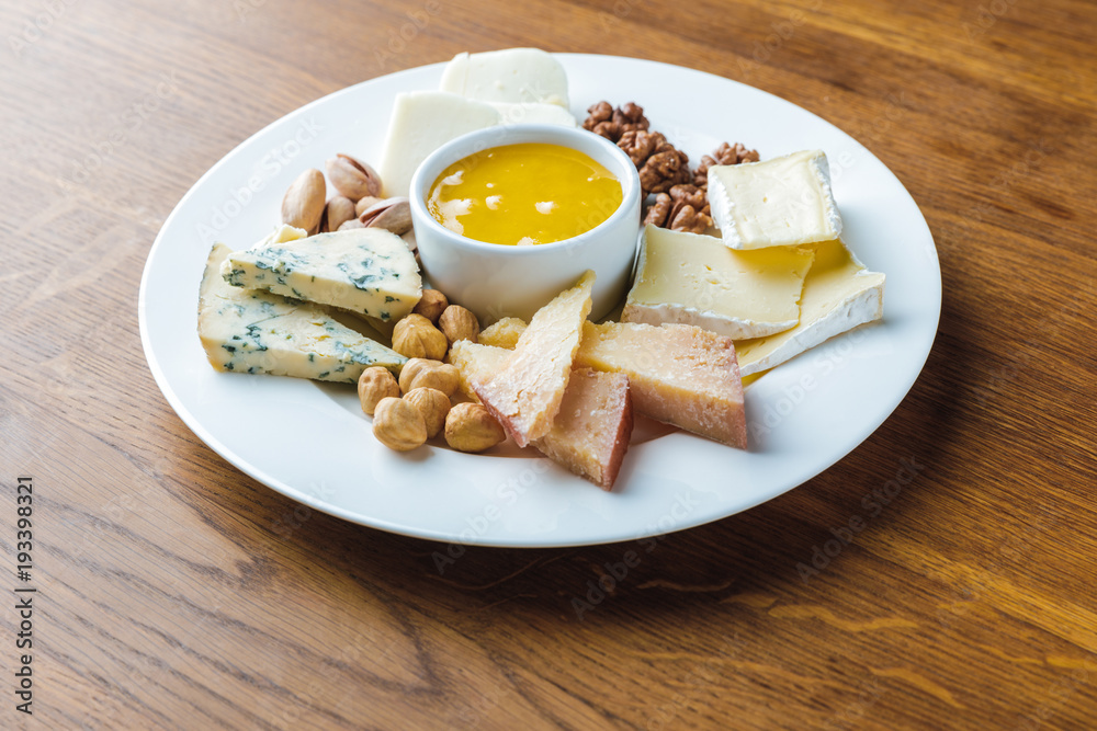 close-up view of delicious cheese plate with nuts and honey on wooden tabletop