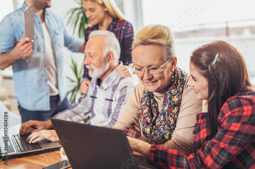 Young volunteers help senior people on the computer. Young people giving senior people introduction to internet © Mediteraneo