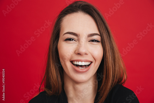 Photo closeup of beautiful adult girl 20s with long brown hair smiling with perfect teeth and looking on camera, isolated over red background