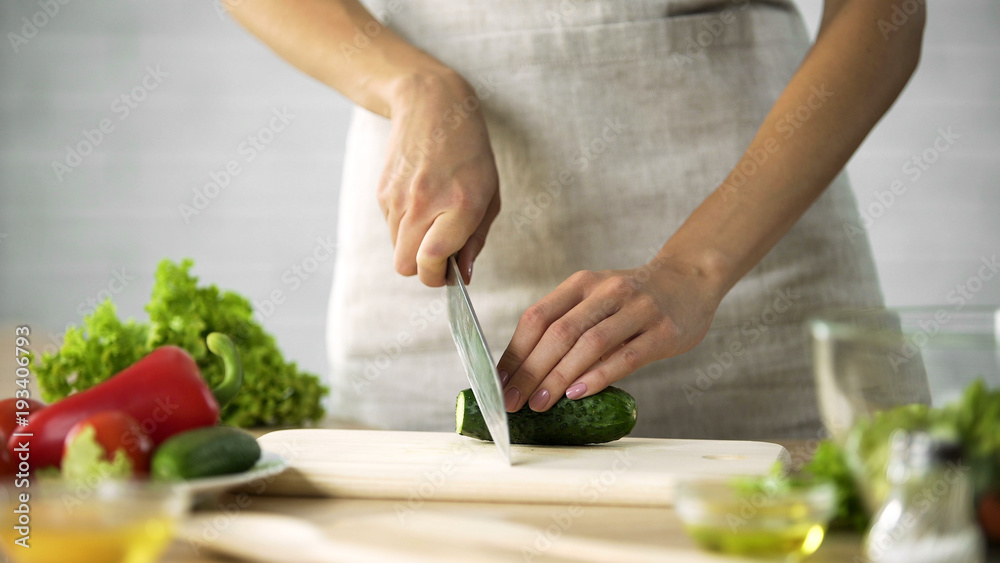Female chef slicing fresh cucumber with a knife on wooden board, vegetables Female chef slicing fresh cucumber with a knife on wooden board, vegetables