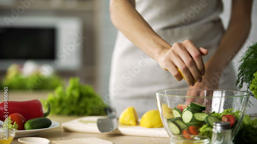 Young cooking girl squeezing fresh lemon juice in salad bowl, vegan, vegetables
