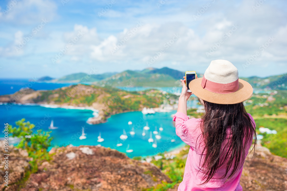 Young tourist woman making photo of English Harbor from Shirley Heights, Antigua, paradise bay at tropical island in the Caribbean Sea