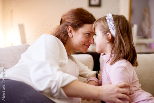 Gorgeous smiling pregnant mother and her joyful little toddler girl daughter looking each other very close.