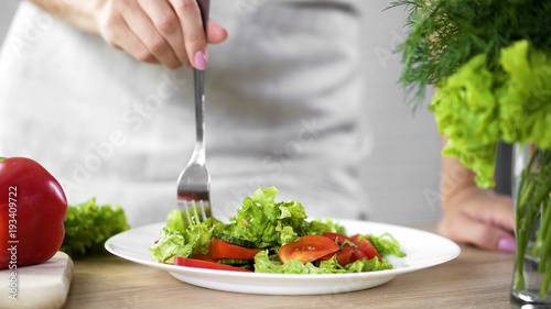 Young woman tasting fresh salad by fork for healthy dinner, fitness lifestyle