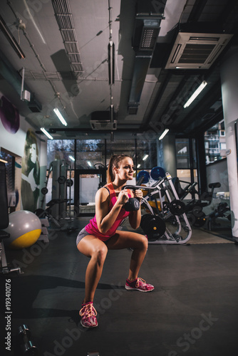 Gorgeous attractive motivated girl doing squats with kettlebell in the gym.